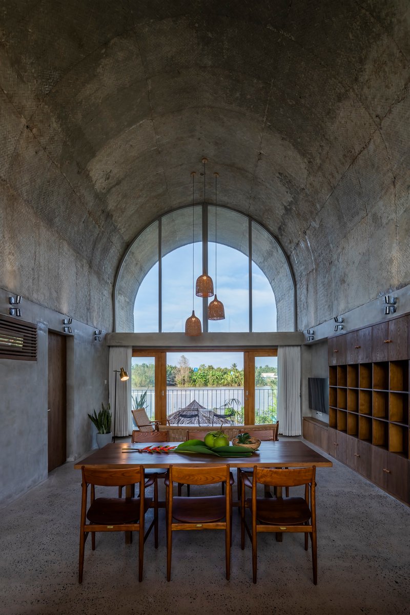 Dining area with vaulted concrete ceiling and arched window framing a view of the water beyond