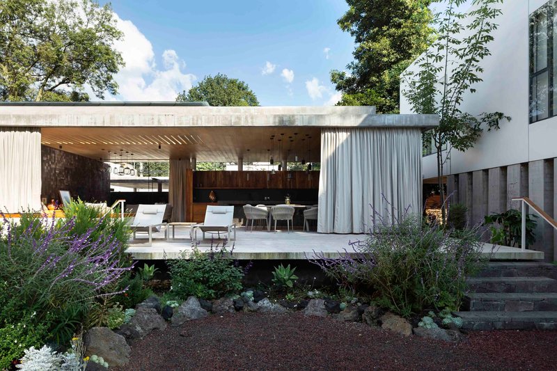 View of the open pavilion across the wild planted garden with curtains drawn back