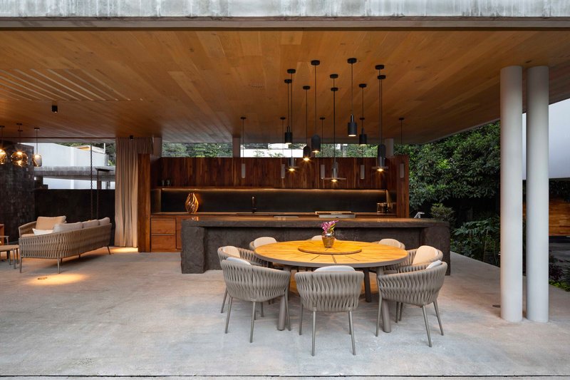 Open dining and kitchen pavilion with a round table, pendant lights and a timber ceiling
