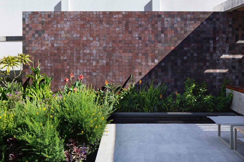 Red volcanic stone tile wall behind a planted bed with bird-of-paradise and grasses