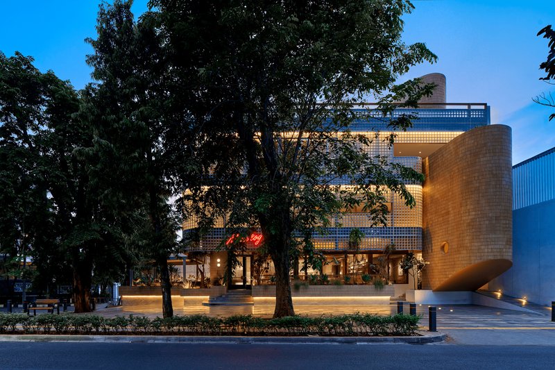 Street view of the glass block facade with cylindrical volume and mature trees at twilight