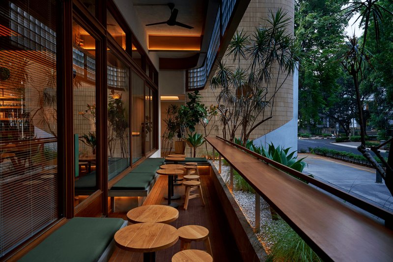 Covered balcony seating area with timber benches and stools under exposed ceiling beams at dusk