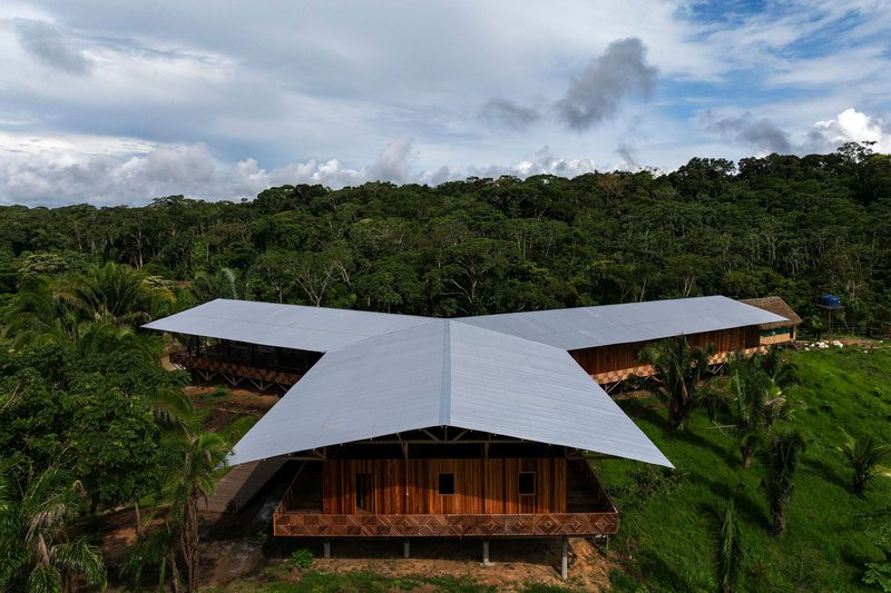 Aerial view of the butterfly-shaped metal roof sheltering a timber structure amid dense rainforest canopy