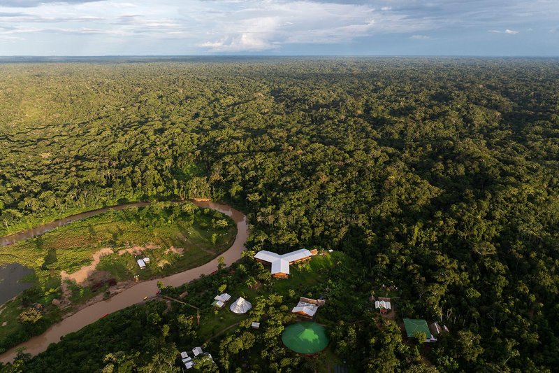 Drone view of the compound with white roofs and scattered pavilions along a meandering river in jungle