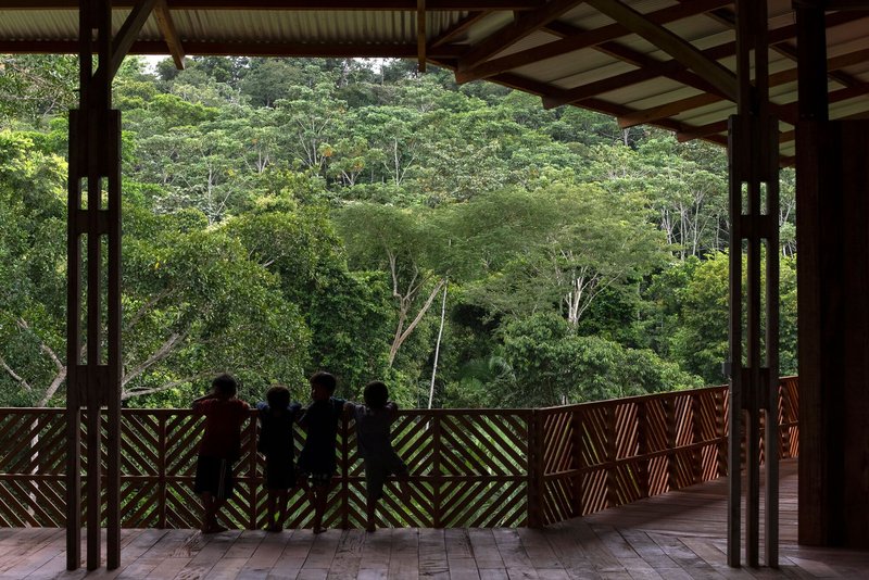 Four silhouetted figures standing at geometric timber balustrade framing dense tropical forest hillside