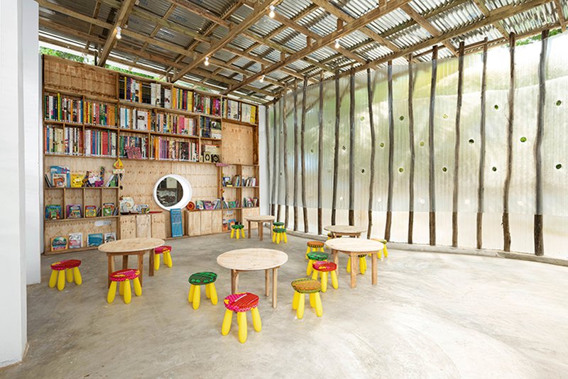 Library interior with plywood shelving along one wall and low tables on polished concrete floor