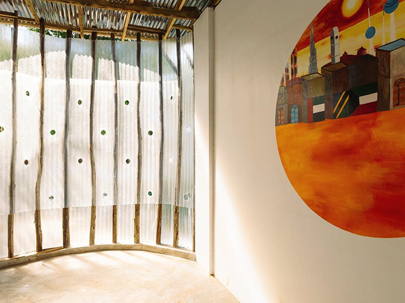 Detail of curved translucent wall with circular glass openings and a painted mural on adjacent surface
