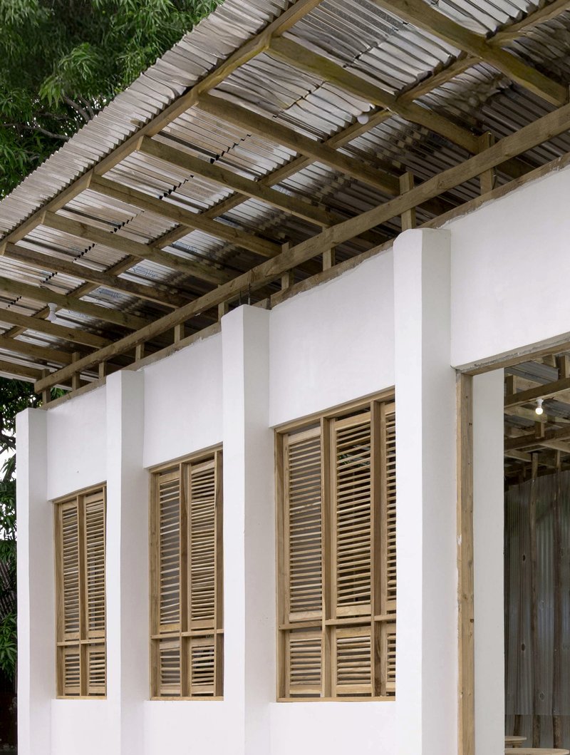 White wall with timber-framed louvered shutters beneath an open timber and corrugated metal roof structure