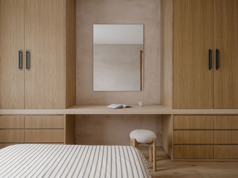 Built-in desk and wardrobe in pale timber with mirror above and striped bedding in foreground