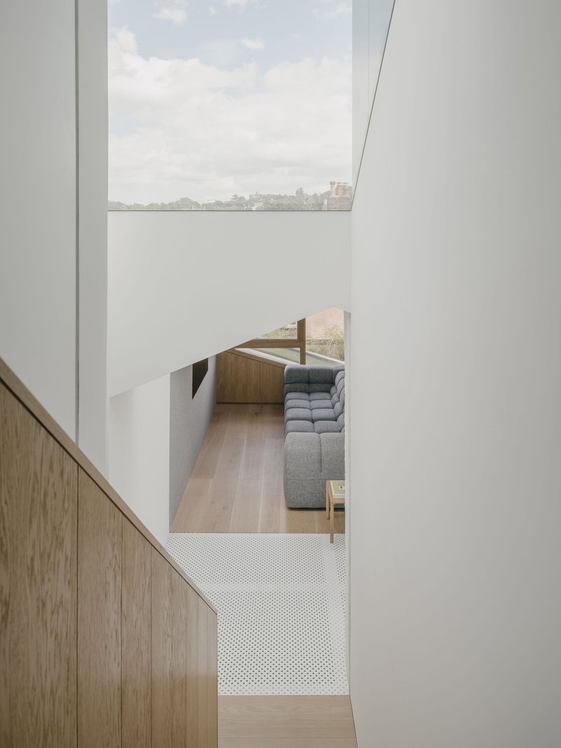View down into a living room with perforated metal floor panel and skylight above