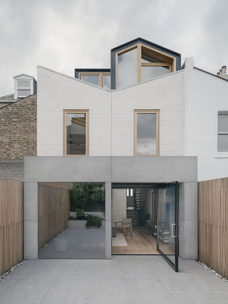 Painted white brick facade with timber-framed windows and glazed courtyard entrance under overcast sky
