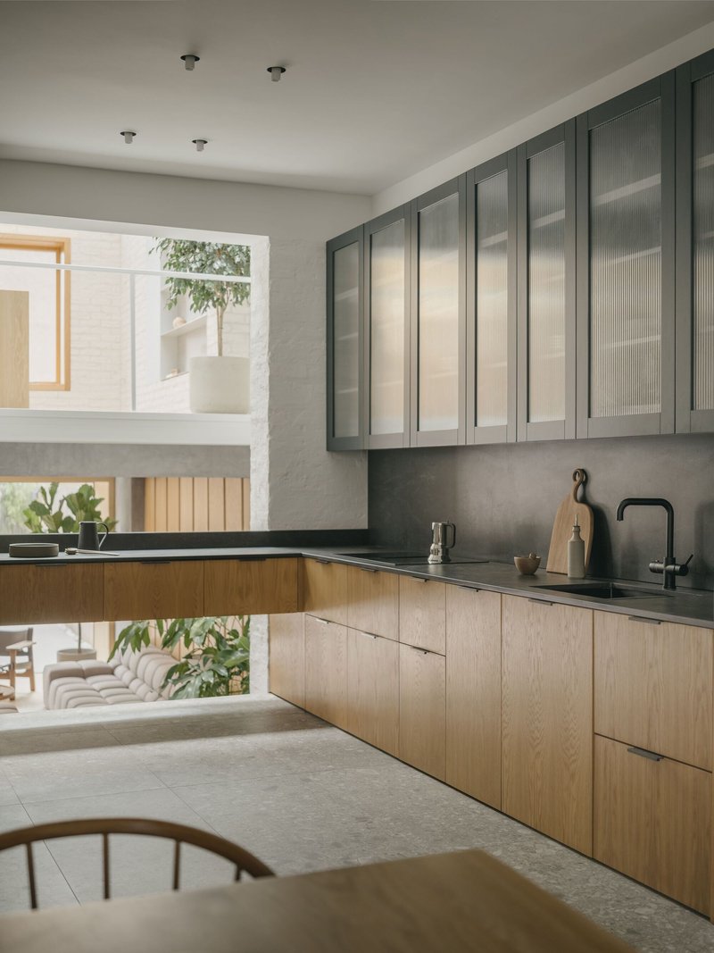 Kitchen with oak lower cabinets and grey upper units framing a double-height void with planted courtyard view