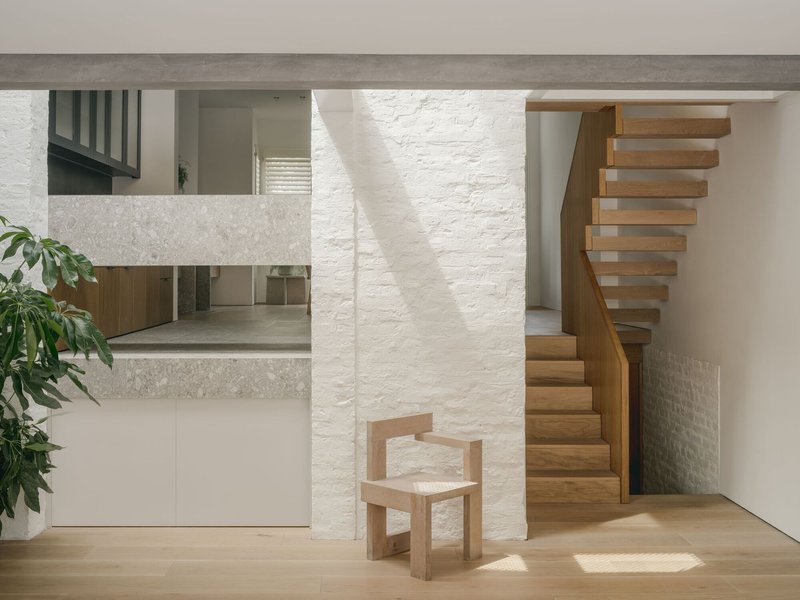 Curved timber staircase beside a painted brick column with afternoon sunlight on timber flooring