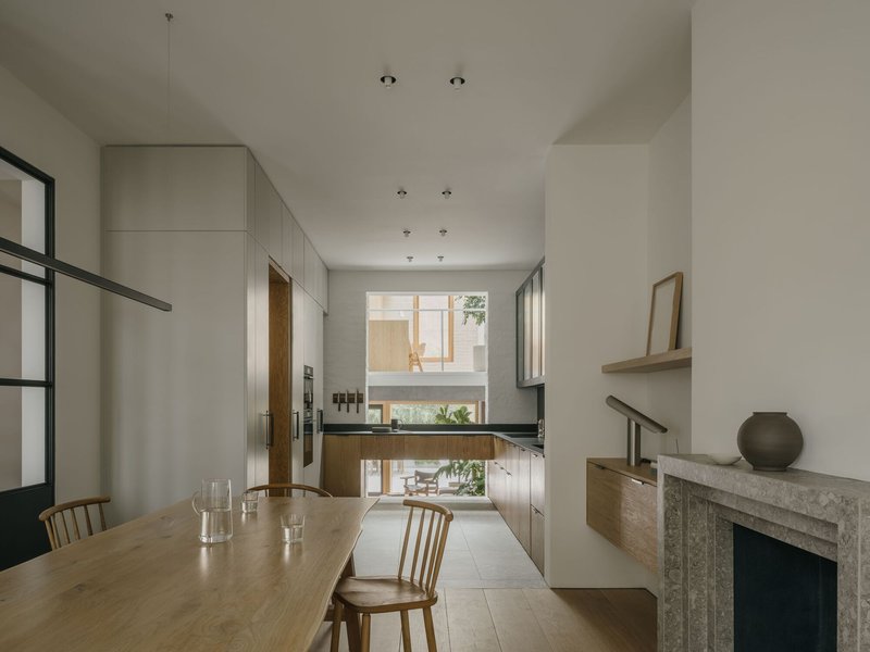 Double-height dining room with timber table and steel-framed glass partition looking onto a courtyard