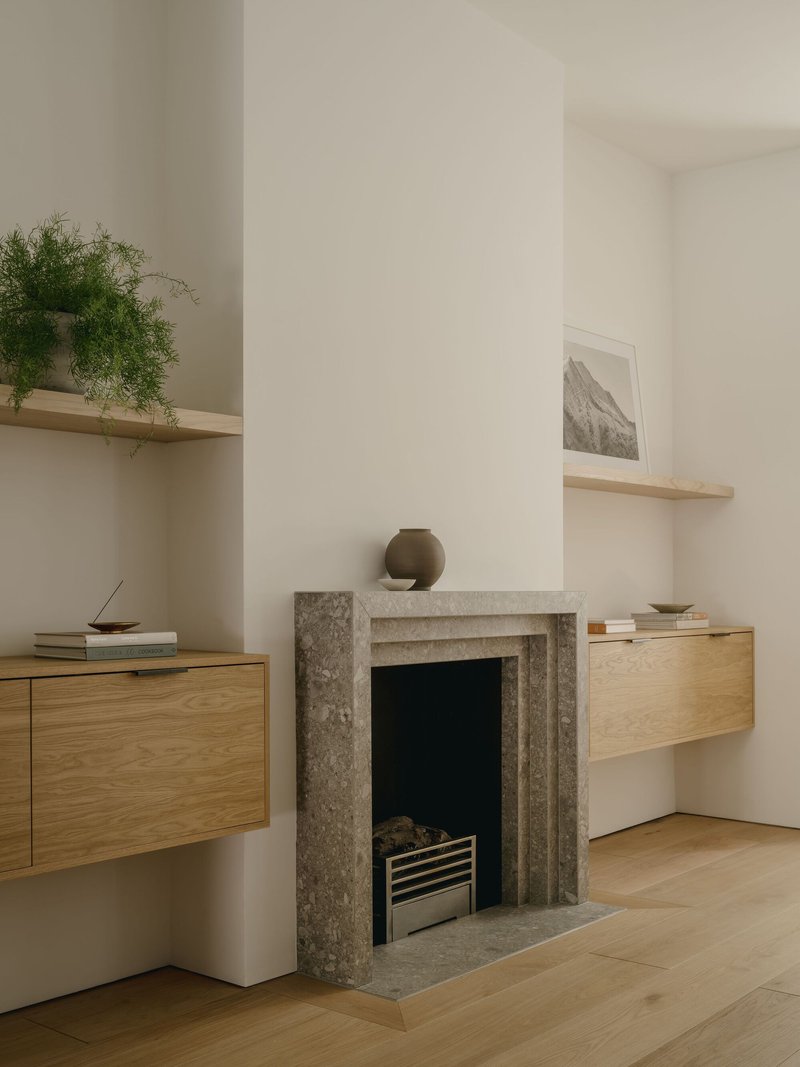 Grey stone fireplace surround flanked by suspended oak cabinetry and floating timber shelves