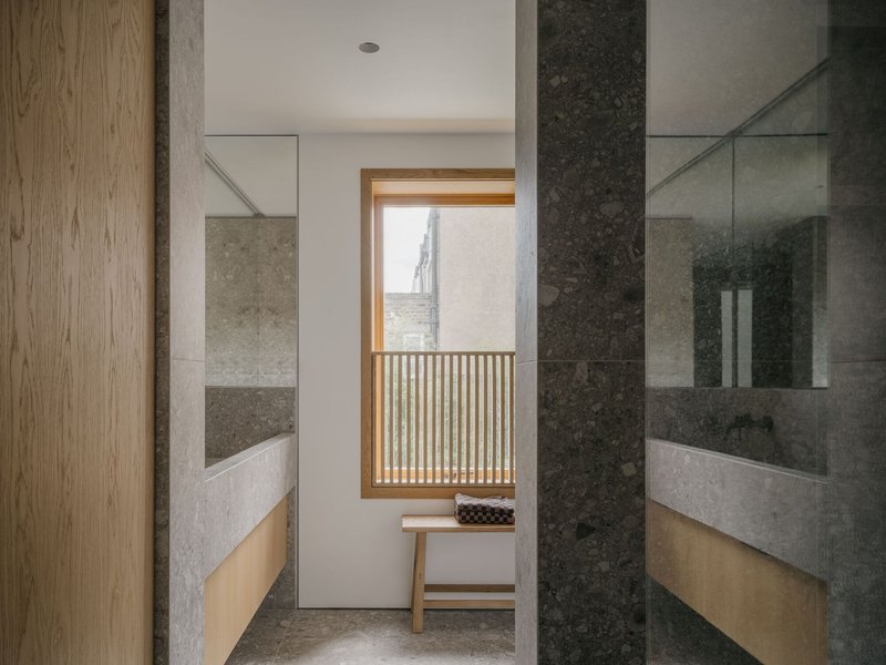 Bathroom corridor with dark and light stone tile walls framing a window with timber screen