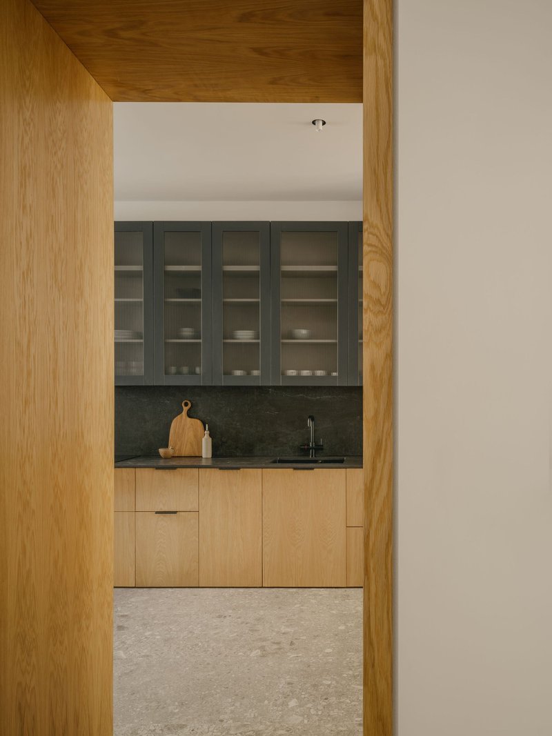 Kitchen viewed through timber-framed doorway with oak cabinetry, dark stone counters and grey upper cabinets