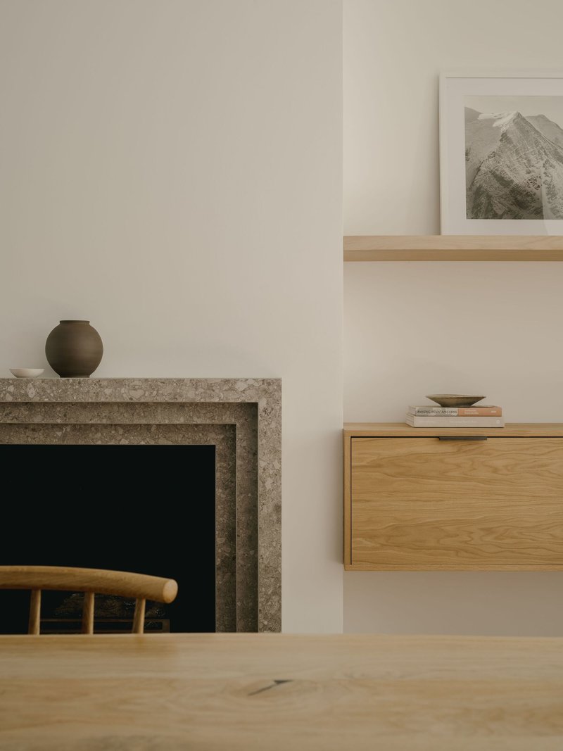 Limestone fireplace surround with oak floating shelves and ceramic vessels in a living room