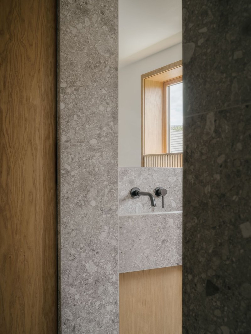 Bathroom sink detail with grey stone walls, timber door and window frame in soft daylight