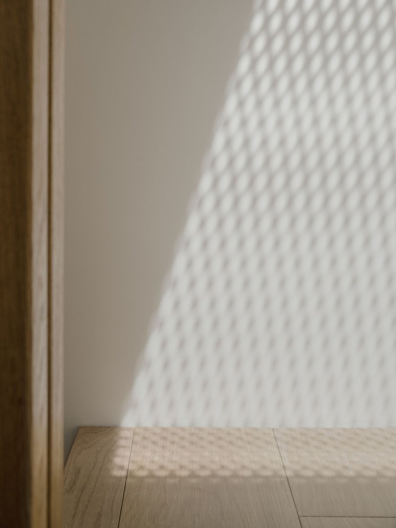 Corner junction where timber floor meets white painted wall beneath filtered window shadow pattern