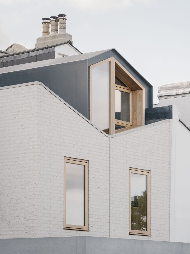 Timber-framed dormer window projecting from dark grey zinc roof above white painted brick facade