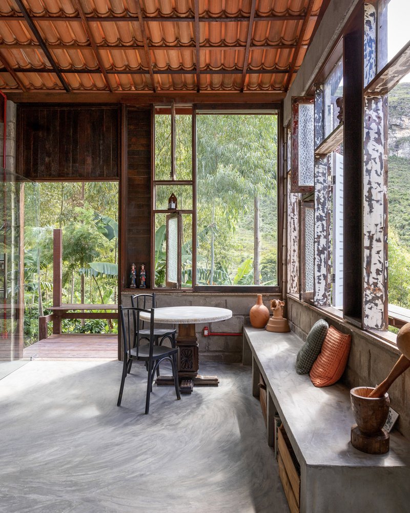 Interior dining nook with built-in concrete bench seating beneath timber-framed windows overlooking lush hillside vegetation