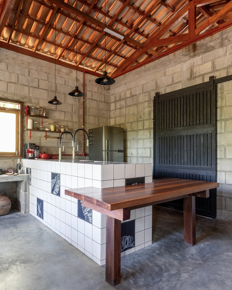 Kitchen island with white tile base, timber countertop and exposed clay tile roof above concrete walls