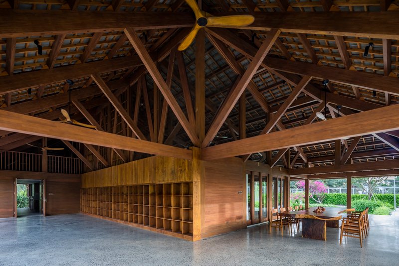 Interior view of exposed timber truss roof structure above a wooden storage unit and dining table