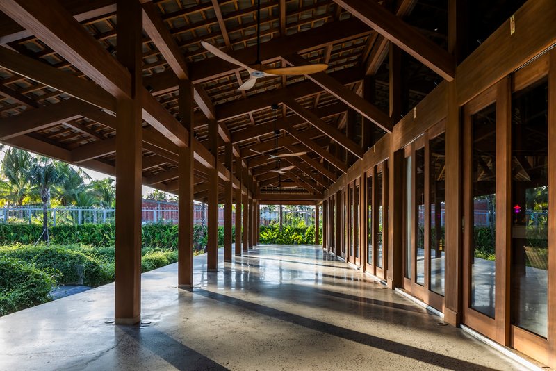 Covered timber colonnade with polished concrete floor and garden views filtering sunlight through columns