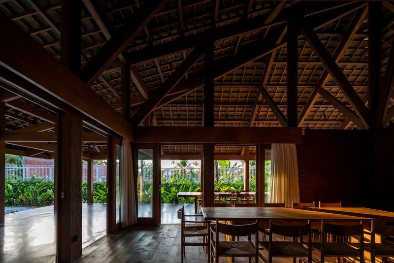 Dining space beneath exposed timber roof trusses with afternoon light filtering through glazed doors