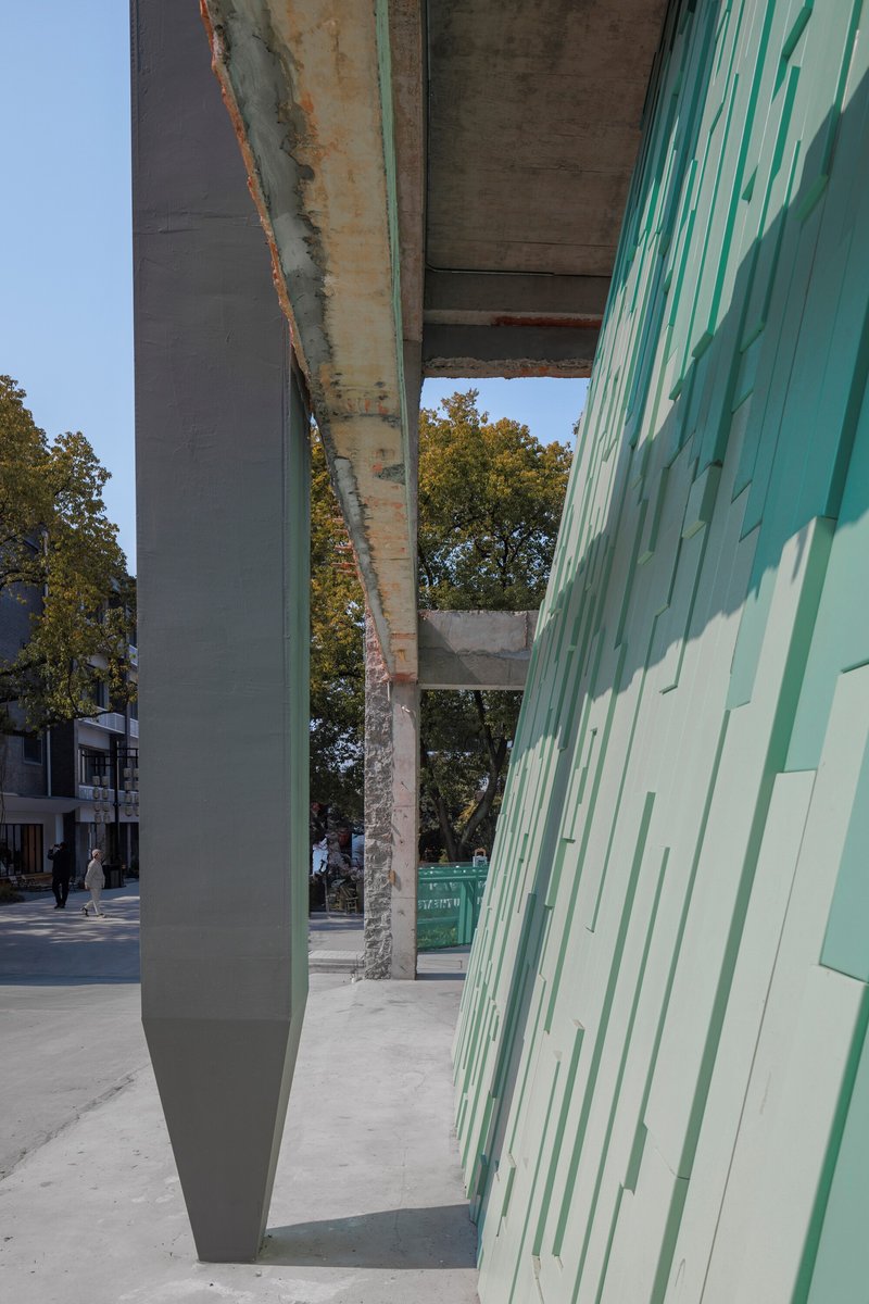 Tapered steel column between the concrete beam soffit and the textured green tile screen
