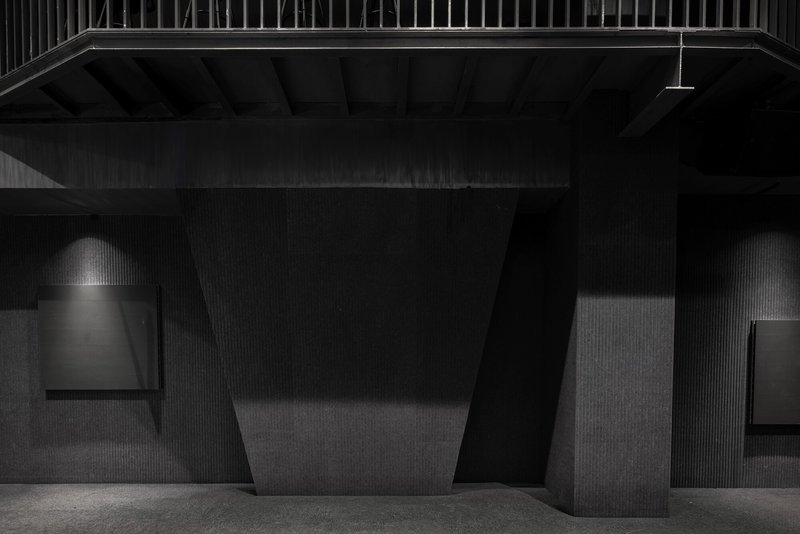 Dark ribbed wall panels flanking a central void with angled structural beams and pendant light