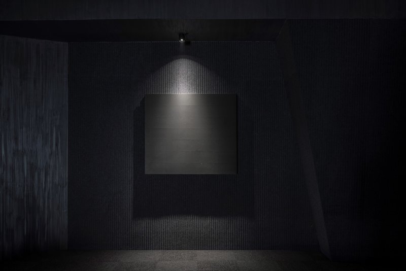 Illuminated display niche framed by black ribbed wall surfaces under a single pendant light