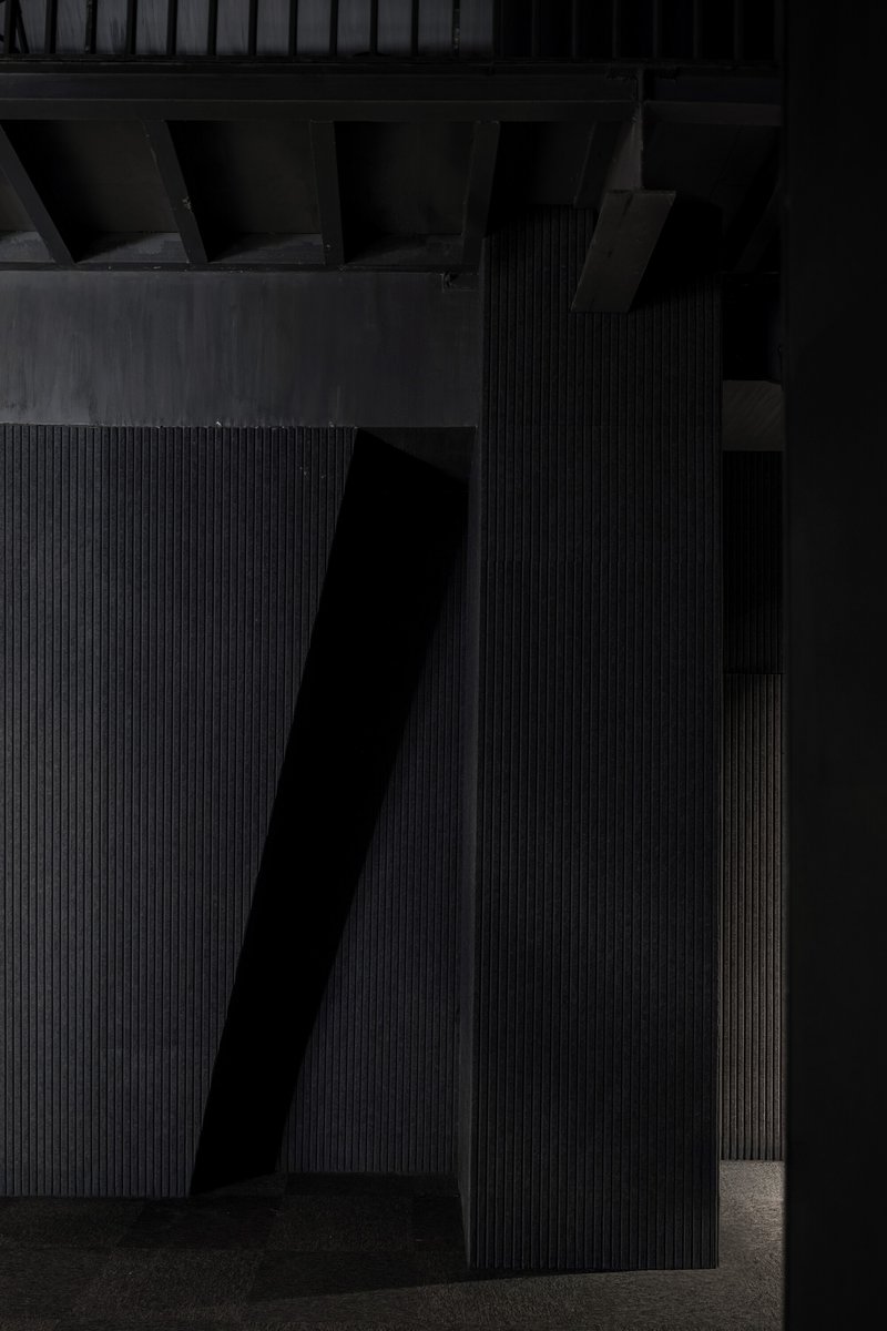 Angled black ribbed wall panels intersecting with an exposed beam ceiling and terrazzo floor