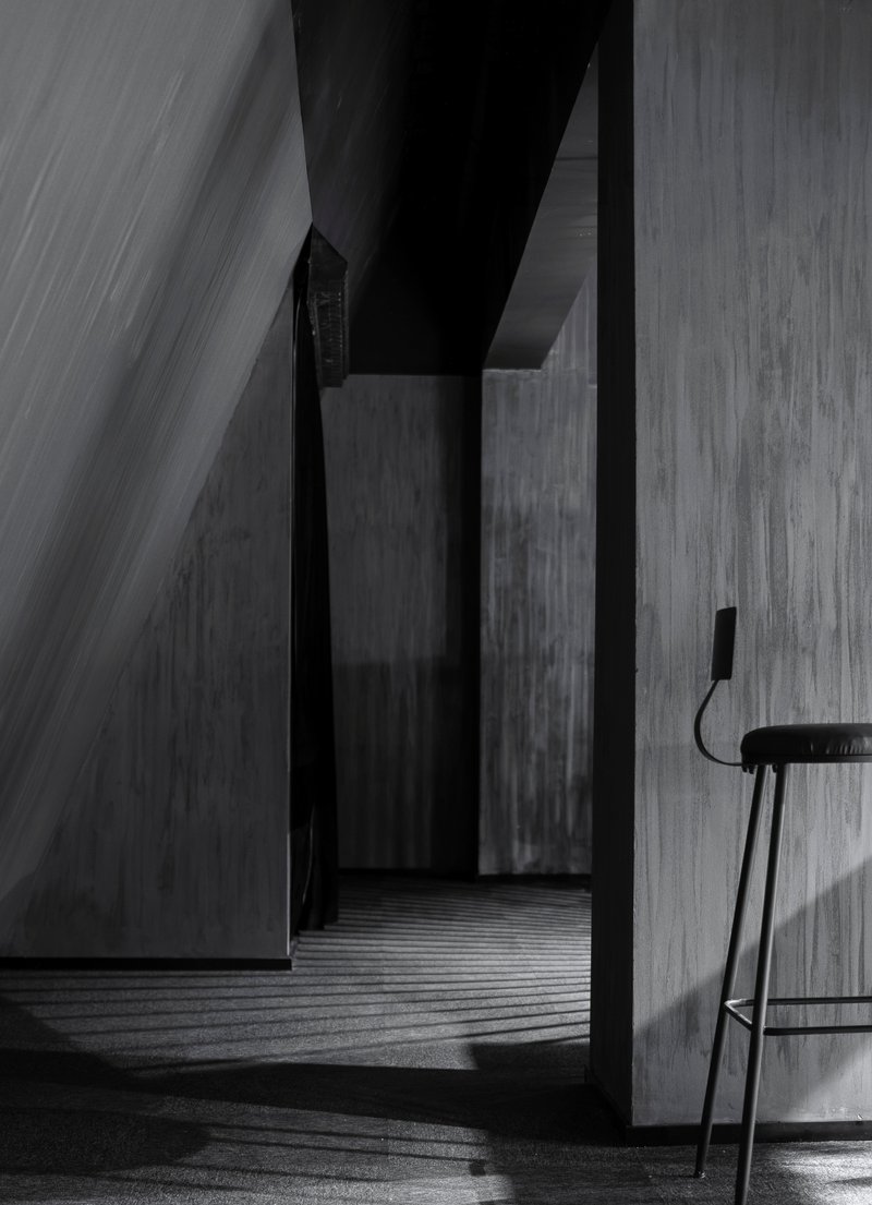 Narrow concrete corridor with angled walls and sharp daylight casting striped shadows across the floor