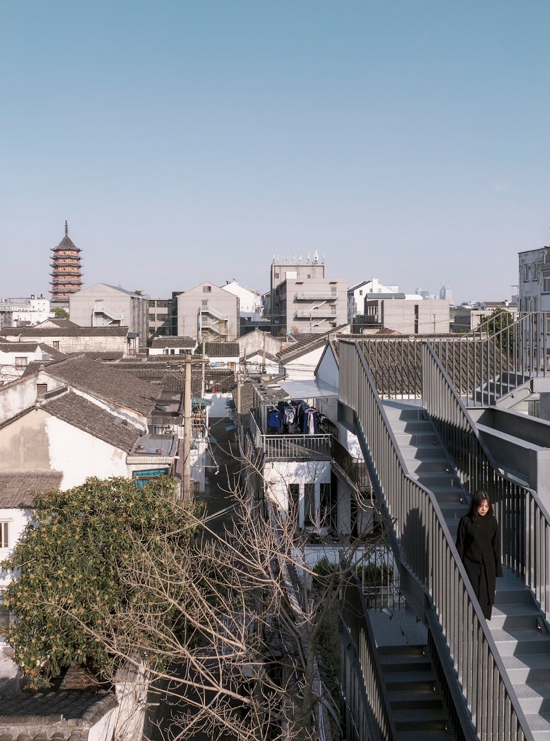 Elevated walkway with metal railings overlooking traditional rooftops and a pagoda tower in the distance