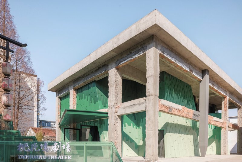 Concrete frame structure with flat roof sheltering the green glass tile volumes between the columns