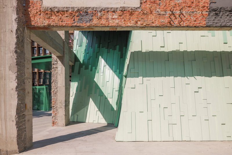 Interior passage through exposed brick and concrete frame with sunlight casting shadows on the glass tiles