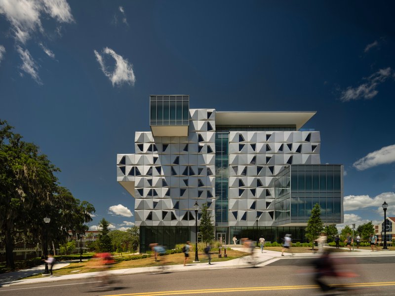 Street corner view showing the stacked volumes with patterned facade panels as pedestrians cross in motion blur