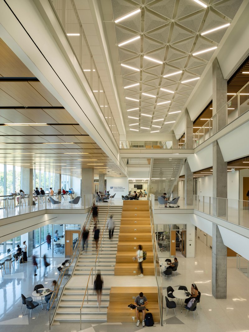 Wide timber staircase with integrated seating beneath a coffered white ceiling and occupied by students