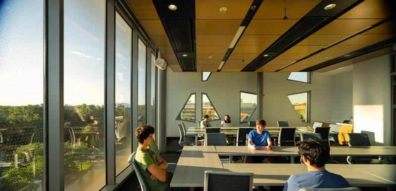 Study desks beneath a wood ceiling with triangular openings framing views to the landscape outside