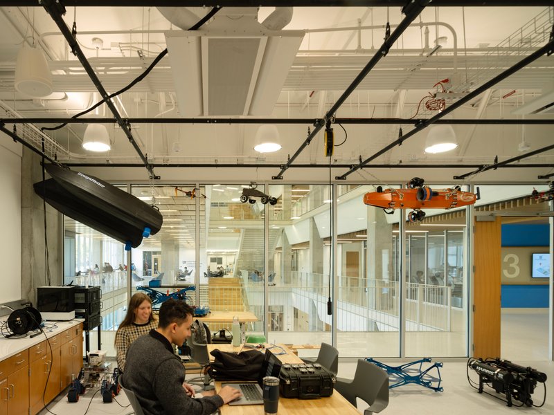 Media production workstation with exposed black conduits and glass partitions overlooking the multi-level atrium