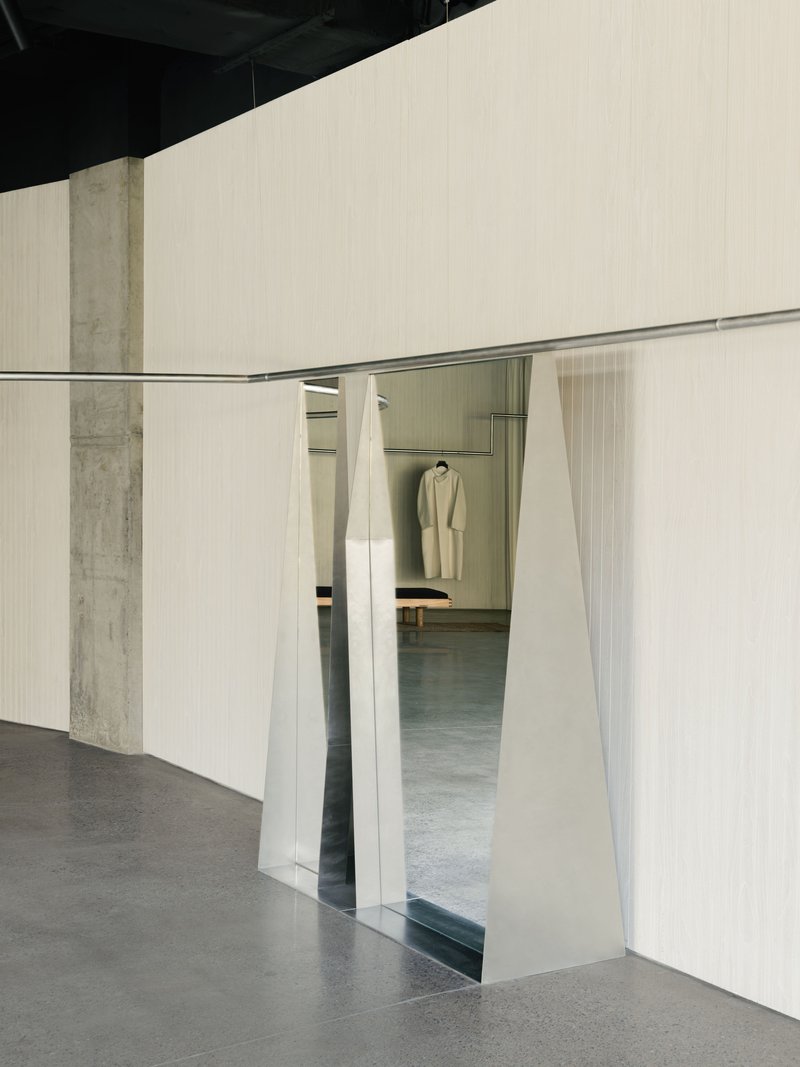 Curved wall opening with splayed metal frame revealing glimpse of hanging garment in next room