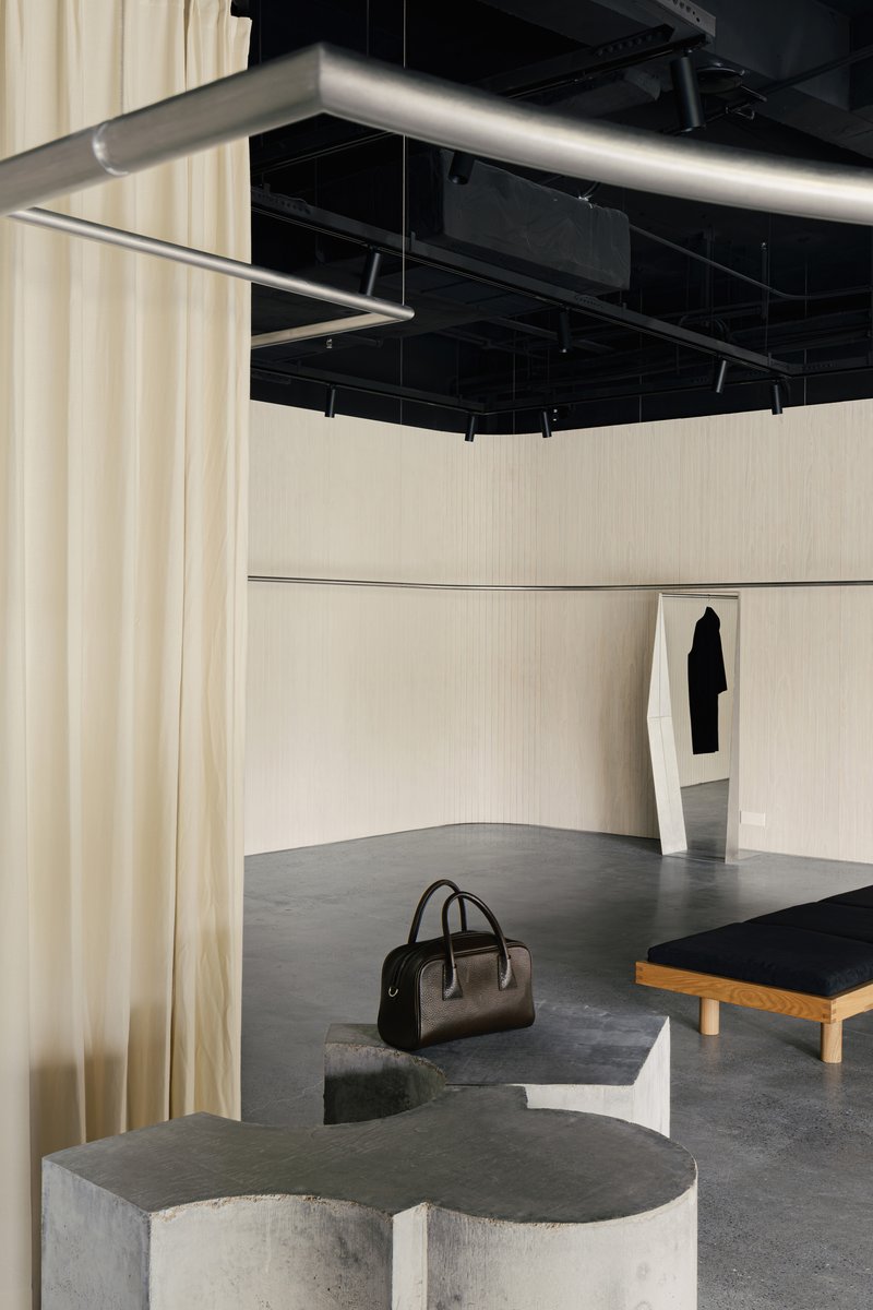 Curved concrete seating plinth with darkened top beneath suspended steel clothing rails and track lighting