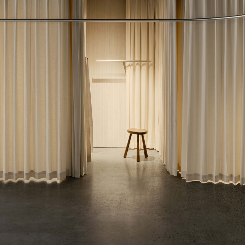 Corridor framed by hanging curtains leading to a wooden stool and coat rack