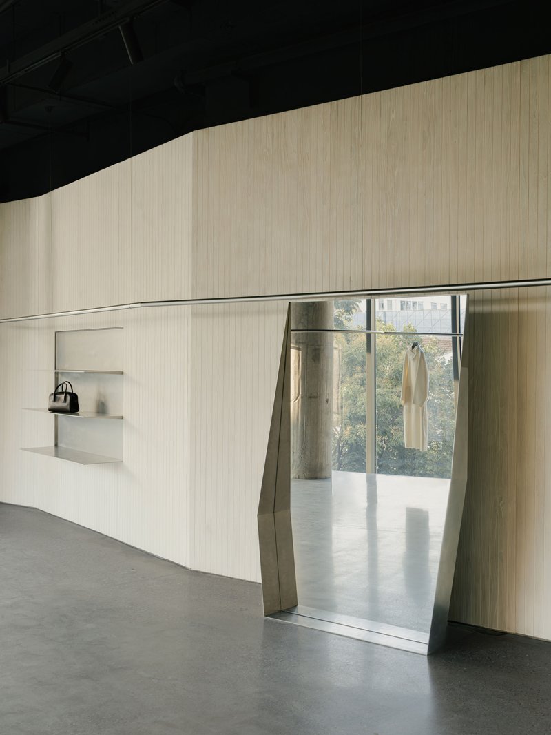 Angled doorway cut through ribbed wall with metal surround leading to daylit space beyond