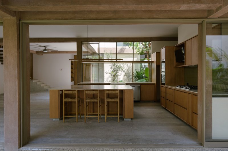 Open kitchen with timber island and stools framed by exposed timber beams and courtyard views