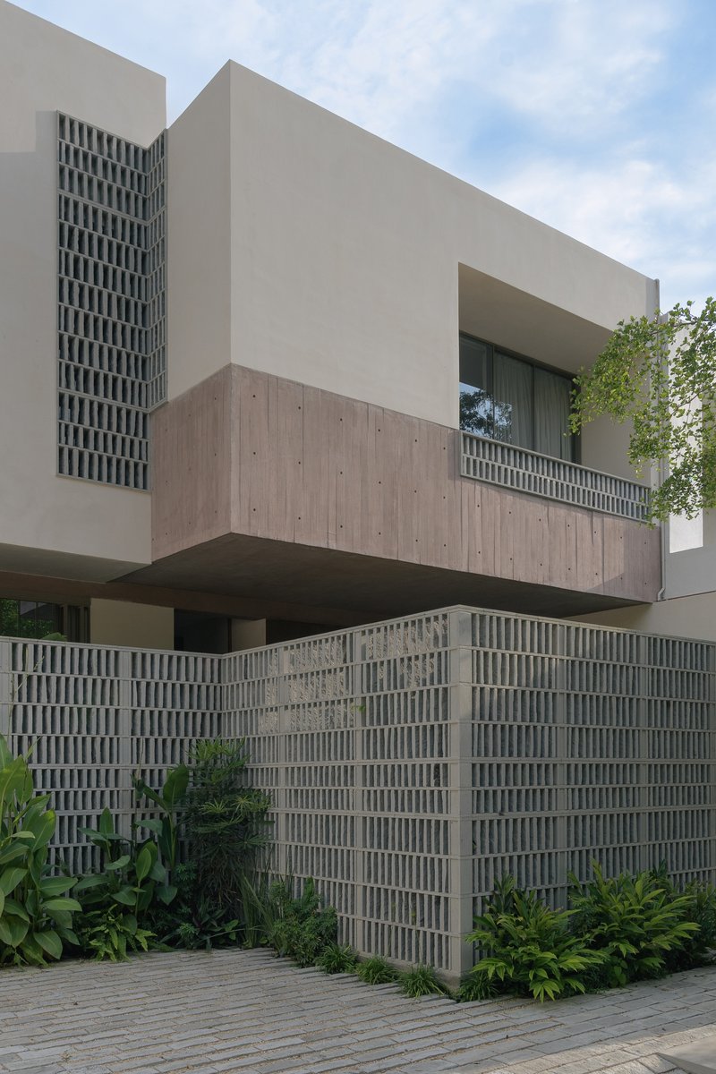 Street facade with cantilevered concrete volume above a perforated block wall and tropical landscaping