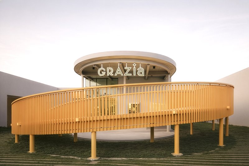 Circular pavilion with vertical timber slat screen and glass dome at dusk
