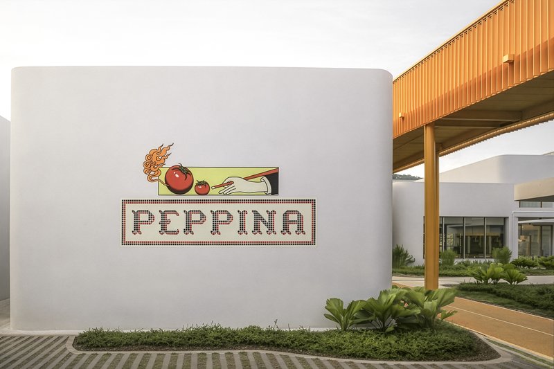 Tiled mosaic signage on white stucco wall beside planted garden beds at dusk